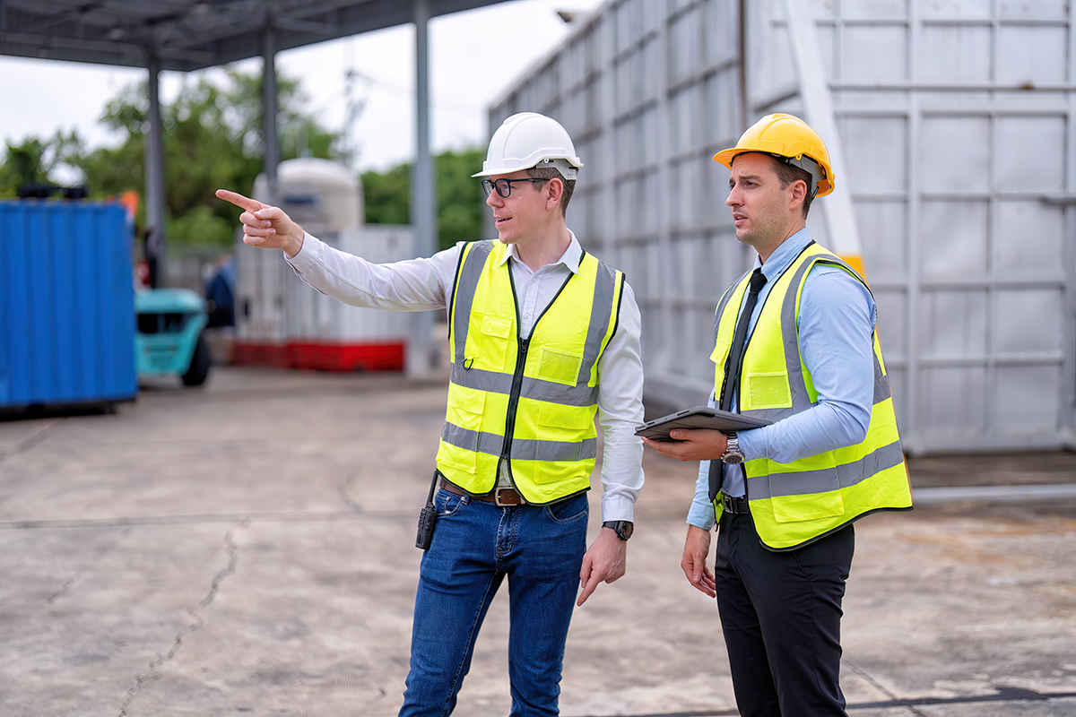 Zwei Männer in Warnwesten und Helmen auf einem Industriegelände